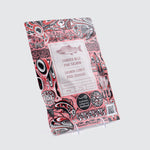 A pink coloured package containing Indigenous Canadian illustrations in red, white and black depicting fish shapes. The centre label showcases a drawing of a salmon with the product name underneath.