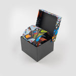 A tie rolled up in its box. The colourful print on the box top matches the print of the tie.