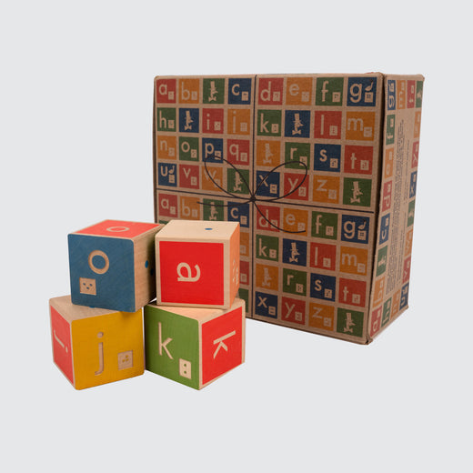 View of the brown cardboard box, with printed images of the blocks covering it. Next to the box are four blocks stacked two by two.