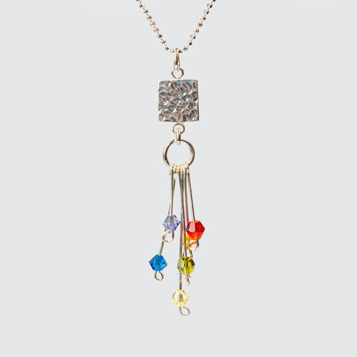 Close-up of the pendant, which is an uneven square of hammered silver and a ring with six rods falling from it and a different coloured crystal on the end of each rod.