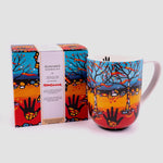 A mug is positioned to the right, with its box to the left. The box features artwork, the artist’s name and the title of the design.