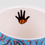 Close-up of a small painted hand in black, with red, orange, and yellow dots on the palm, located on the inside lip of the mug.