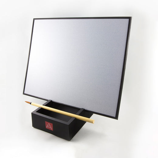 Grey board angled upright and resting in the groove of a black tray; a paint brush rests in the tray