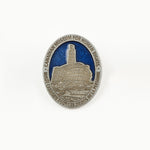 oval-shaped pewter-coloured pin featuring an image of the CMHR against a blue sky