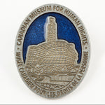 oval-shaped pewter-coloured pin featuring an image of the CMHR against a blue sky