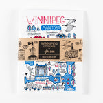 Notebook wrapped with a kraft brown paper band with the text “Winnipeg Cityscape by Julia Gash Notebook” 