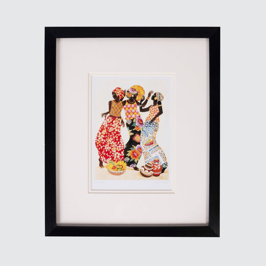 Art print in a black frame featuring three Black women who appear to be dancing under the sun with baskets of food at their feet.