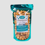 A metallic teal blue plastic bag with clear front and a label including the Utoffeea name and logo, as well as a drawing of the Canadian Museum for Human Rights. The bag is filled with toffee popcorn drizzled with chocolate.
