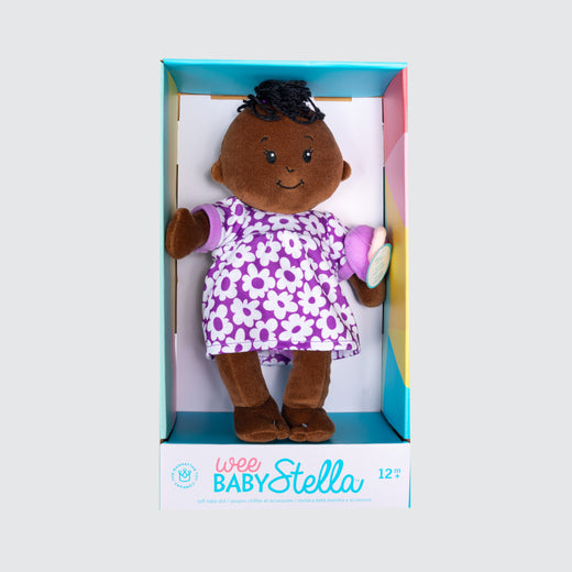 Une poupée en tissu à la peau foncée avec une queue de cheval noire sur le dessus de la tête. La poupée est habillée d’une robe violette et blanche avec une sucette assortie.